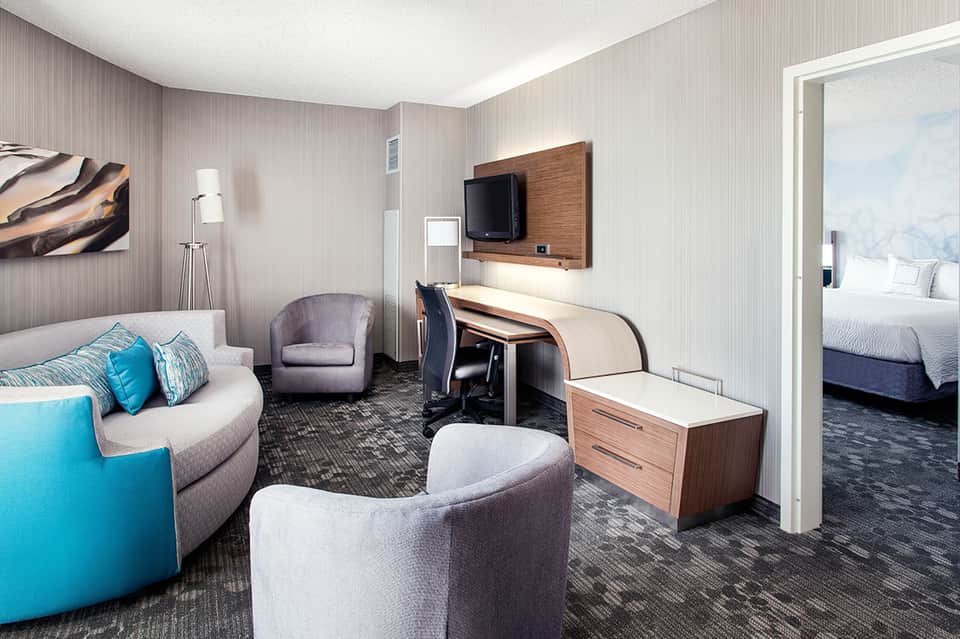 Hotel suite living room with curved sofa, TV, and bedroom doorway