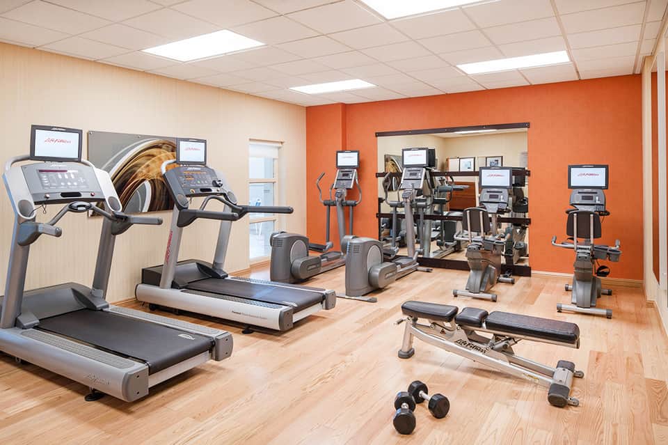 Fitness center with orange accent wall, treadmills, ellipticals, weights, and exercise equipment