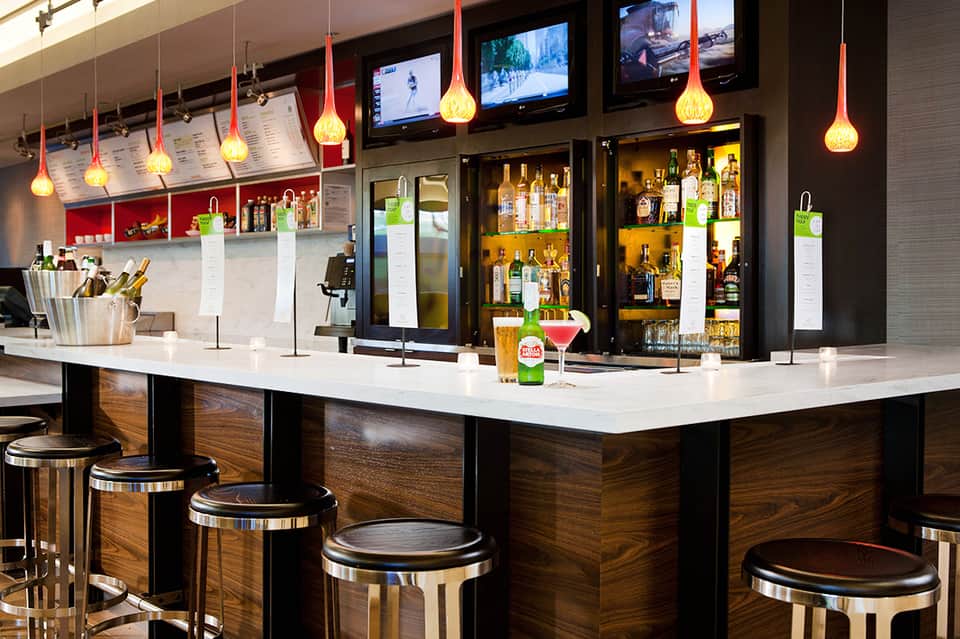 Contemporary hotel bar with wood accents, backlit bottles, and gold pendant lighting