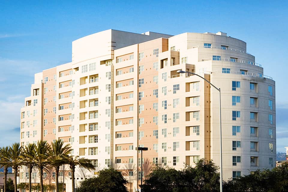Contemporary mid-rise hotel building with curved corner, peach and white facade, and palm trees