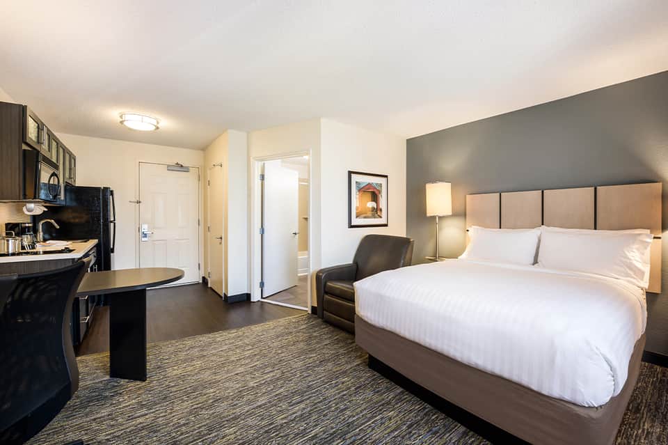 Hotel bedroom with queen bed, kitchenette area, work desk and modern furnishings