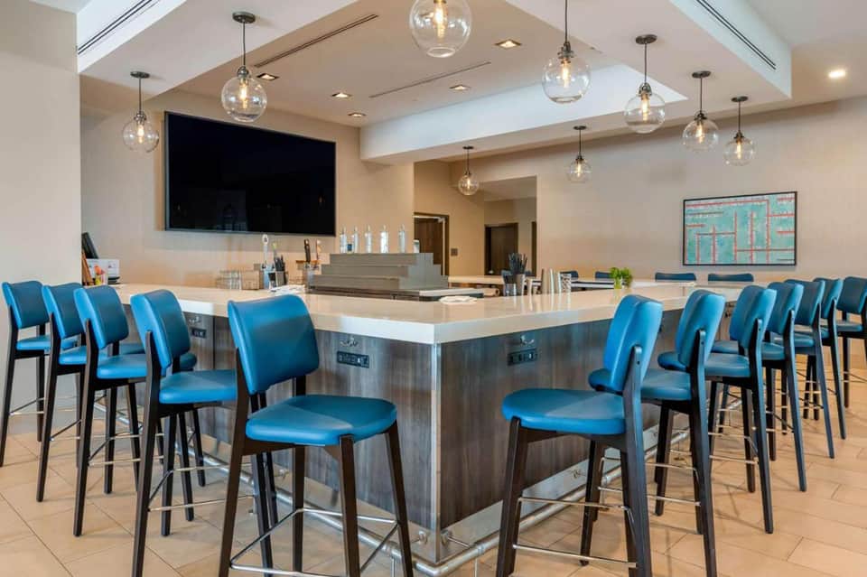 Hotel conference room with u-shaped seating, blue chairs, pendant lights, large screen, and bar counter