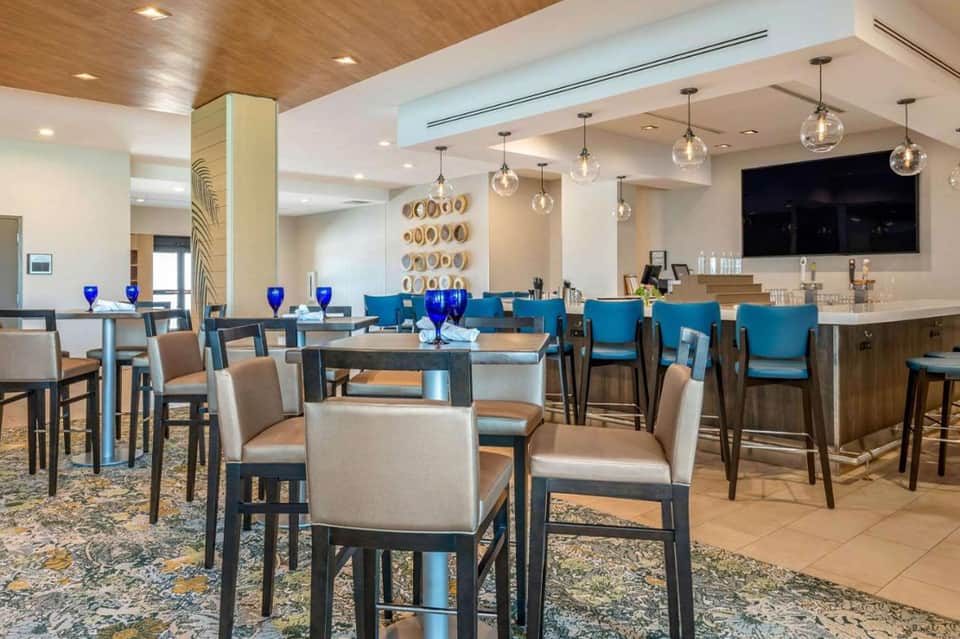 Modern restaurant and bar lounge with turquoise bar seating, high-top tables, and pendant lighting