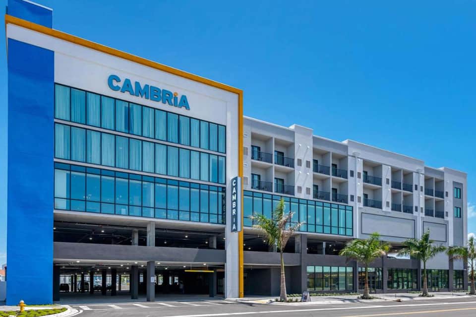 Modern Cambria hotel exterior with blue facade, parking structure, and palm tree landscaping
