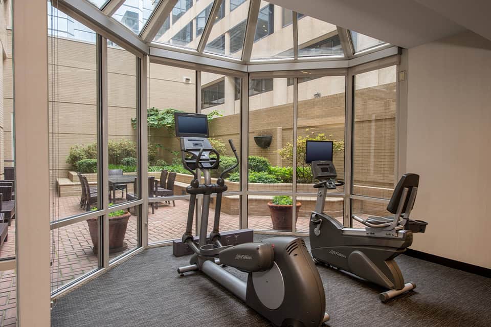 Indoor fitness center with exercise bikes and windows overlooking urban courtyard