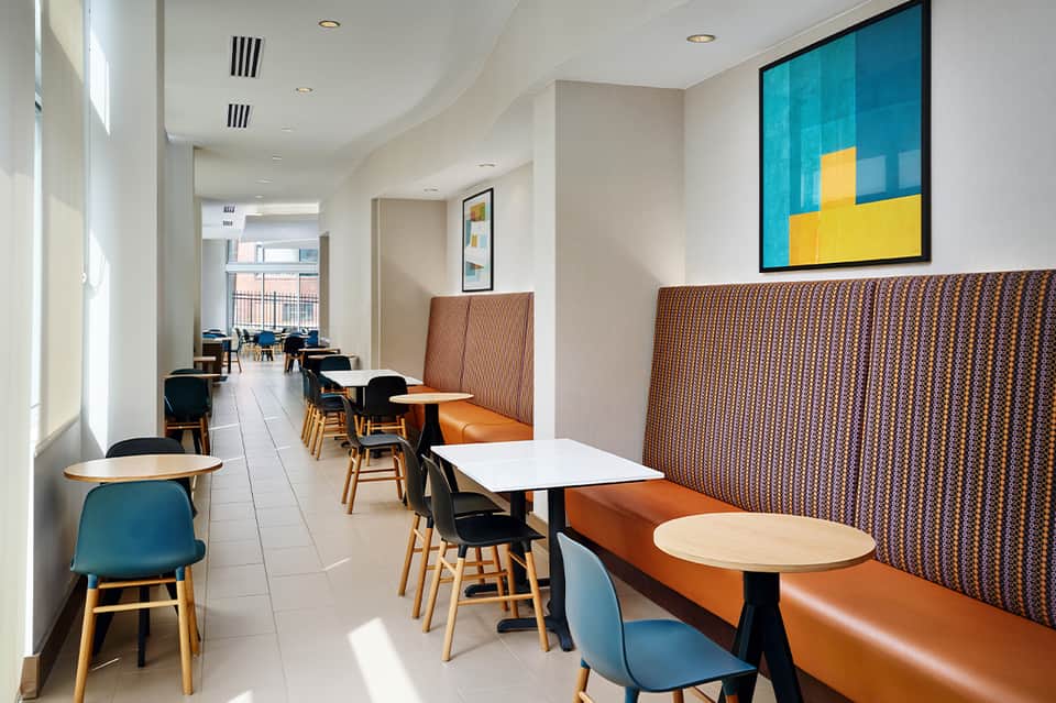 Modern hotel café with orange leather booths, wood chairs, and turquoise wall art