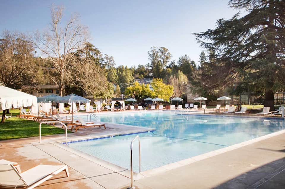 Expansive resort pool with multiple sections, lounge chairs, white cabanas, and tree-lined landscape
