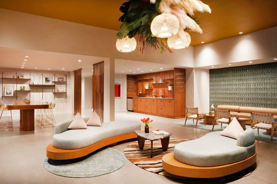 Modern resort lobby with curved seating, orange accents, woven pendant lights, and wooden elements