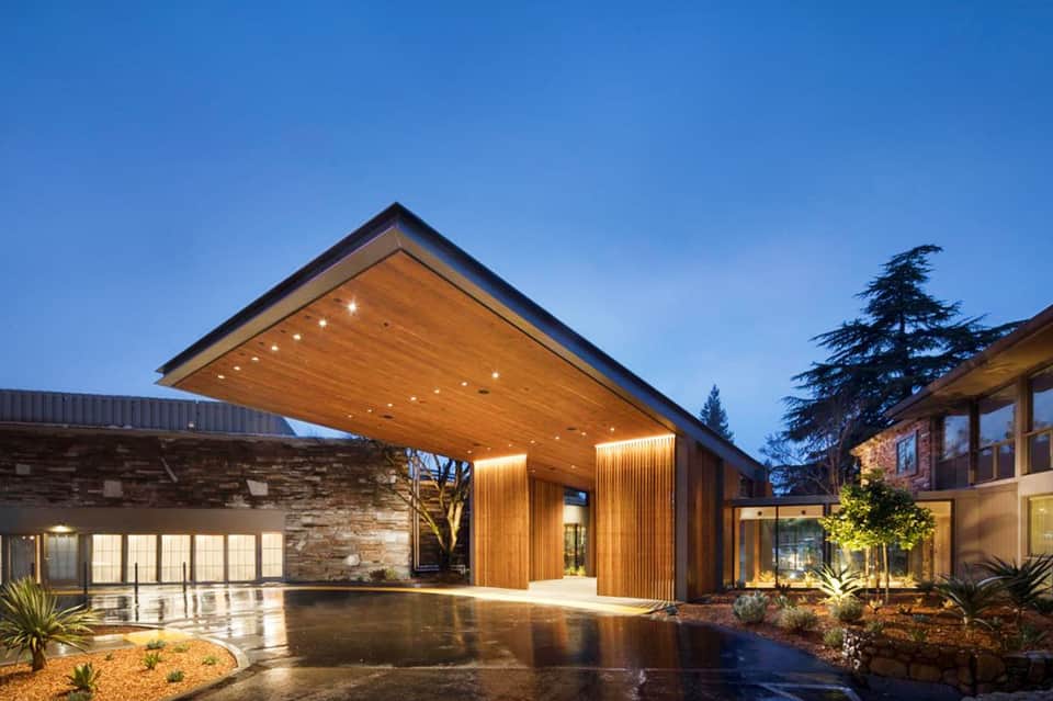 Modern residential courtyard with wooden canopy, stone walls, and uplighting at twilight