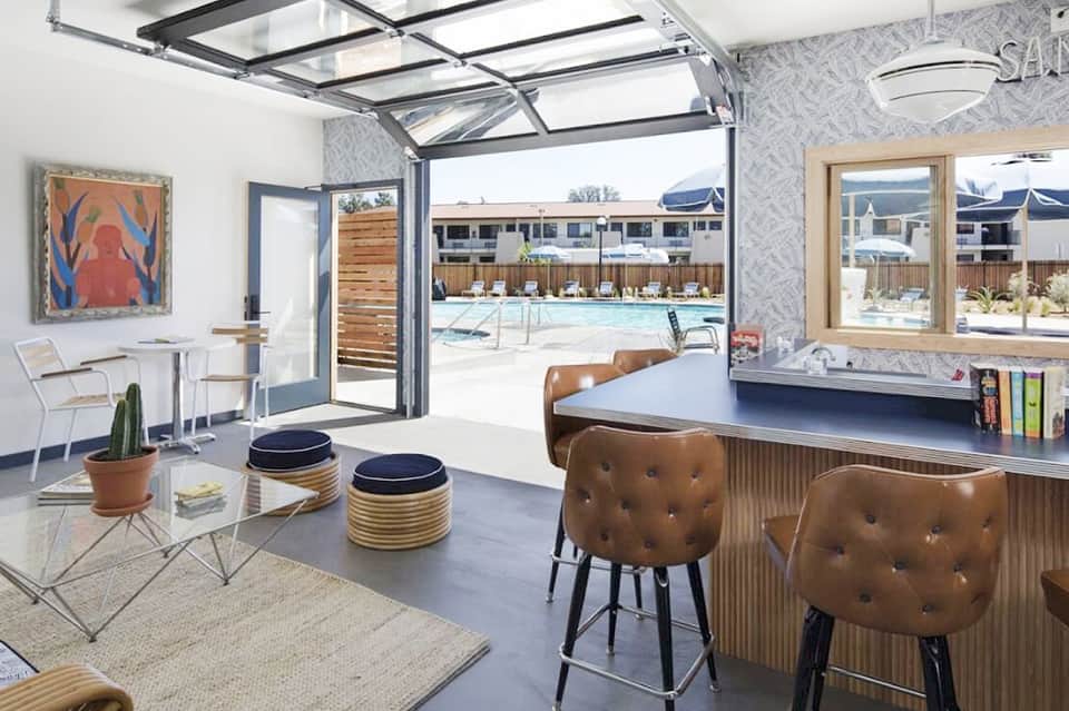 Modern resort lobby with open glass doors overlooking pool, featuring leather bar seating and bright decor