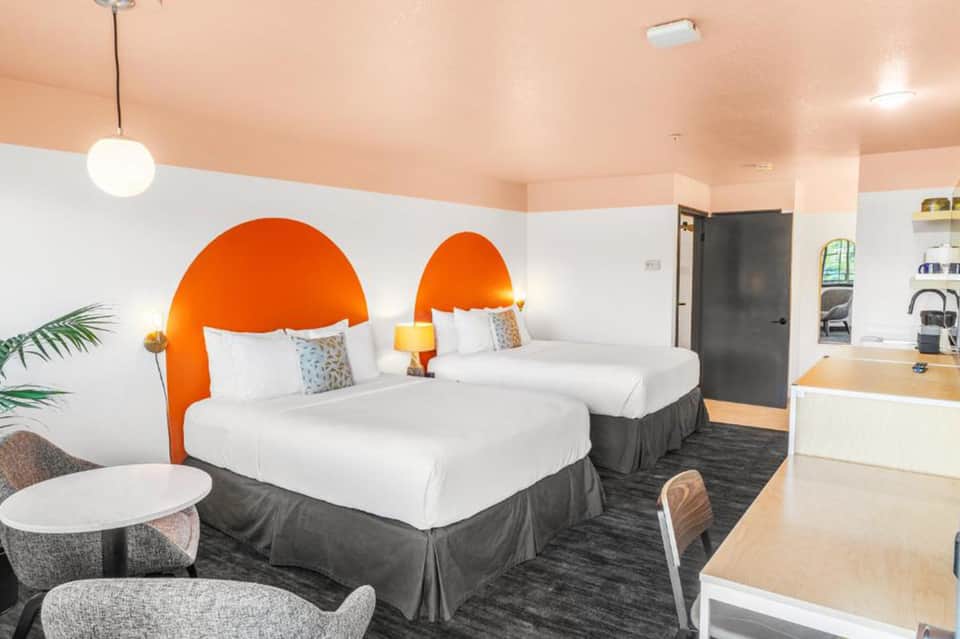 Contemporary hotel room with two queen beds, bold orange headboards, white bedding, and modern furnishings
