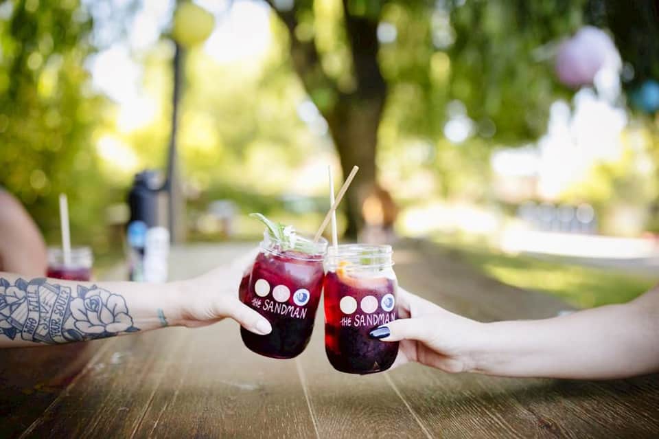 Two hands toasting with mason jars of dark beverage outdoors in natural setting