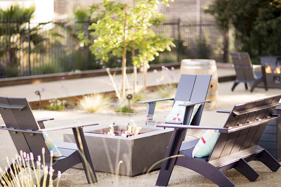 Modern rooftop lounge with fire pit, Adirondack chairs, trees, and city skyline view