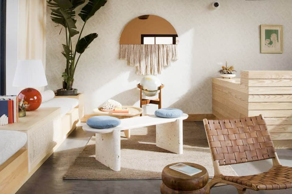 Minimalist bedroom with white furniture, macramé wall art, blue cushions, and wooden accents