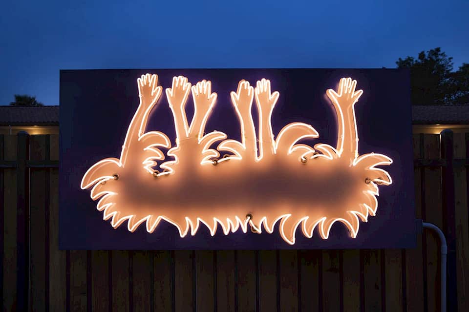 Neon sign artwork depicting glowing orange hands against dark background at dusk