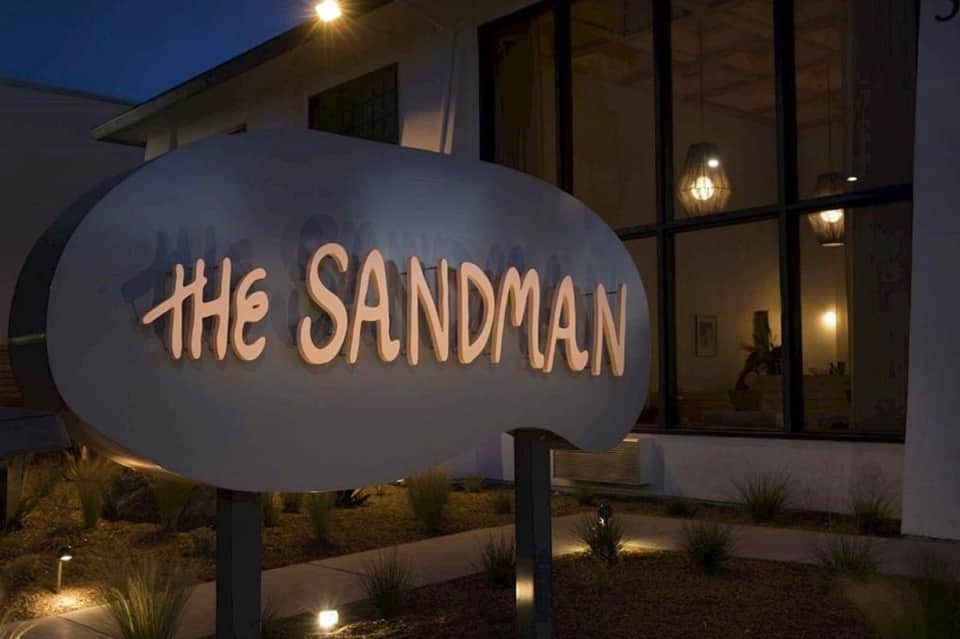 The Sandman hotel illuminated sign at night with modern building entrance and landscaping