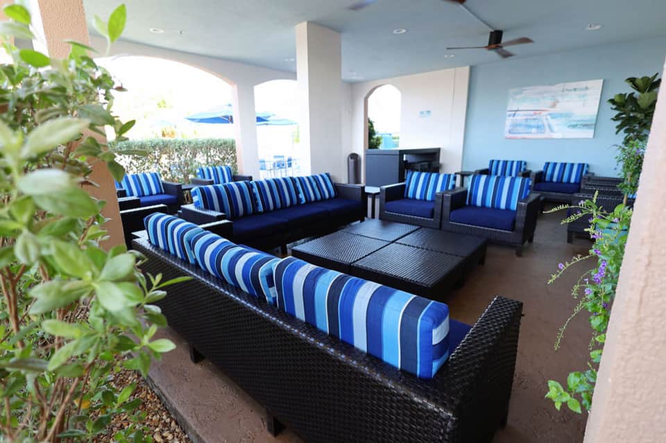 Modern covered lounge area with blue striped seating, plants, and ocean view in background