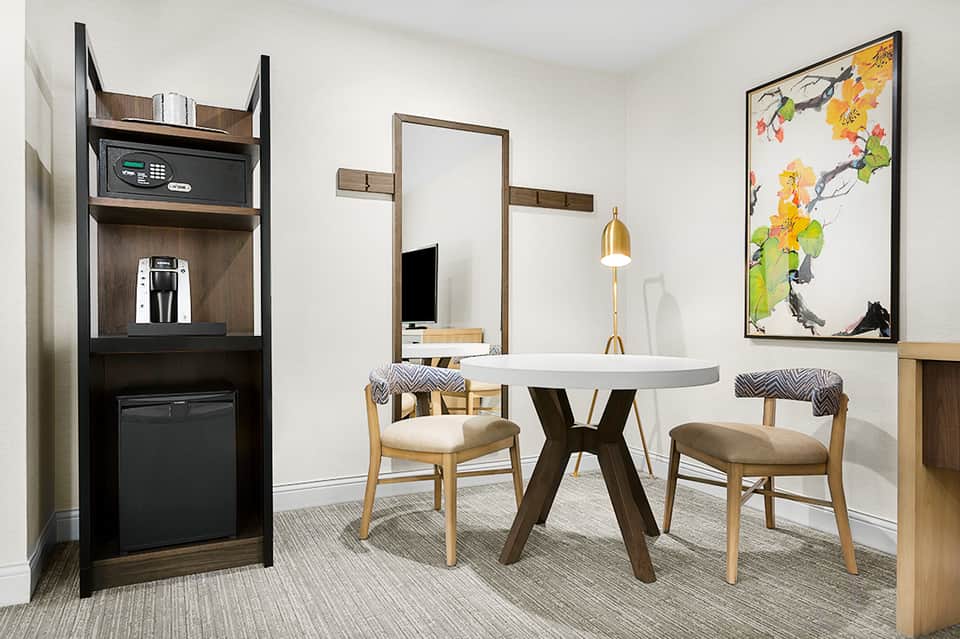Modern suite interior with round dining table, chairs, wall-mounted mirror, and amenities