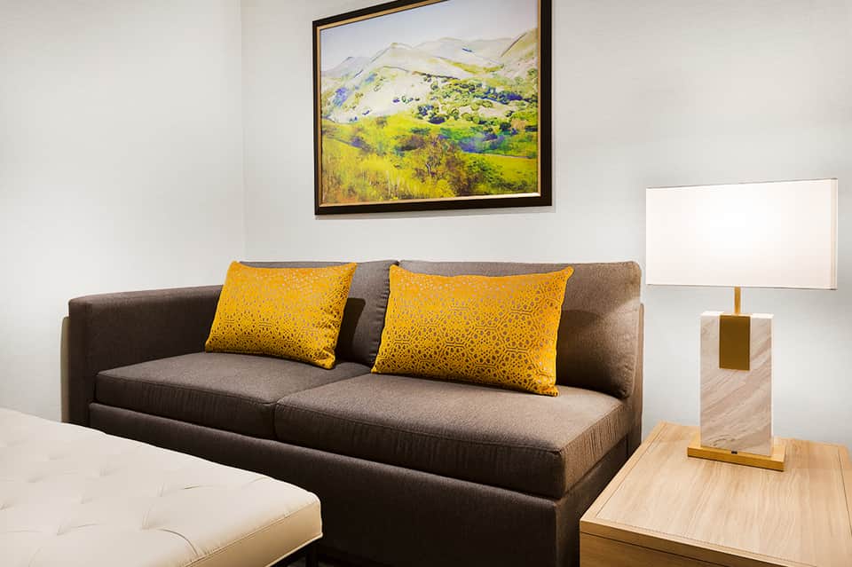 Modern hotel suite living room with gray sofa, yellow pillows, and landscape artwork