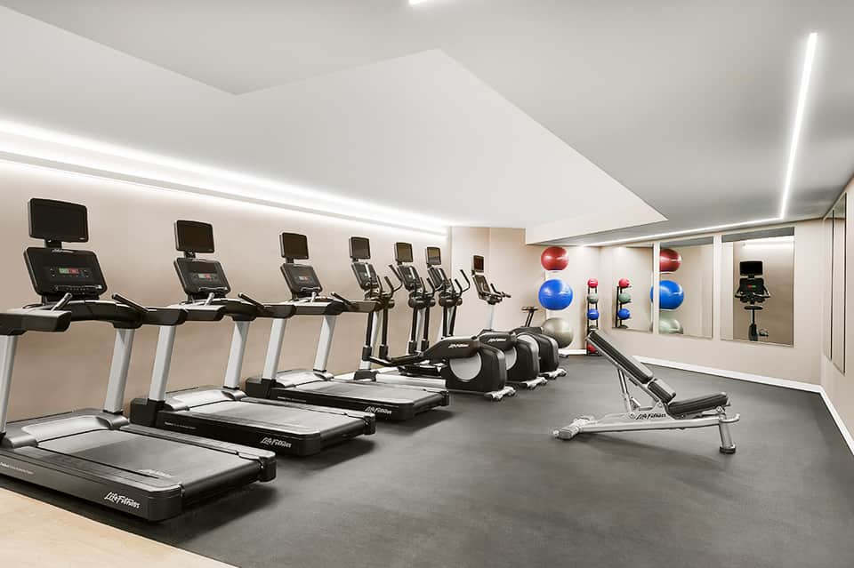 Modern hotel fitness center with treadmills, stationary bikes, dumbbells, and exercise balls