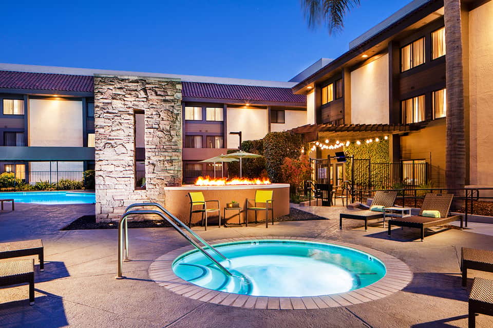 Resort courtyard at dusk with spa tub, fire pit, and illuminated buildings