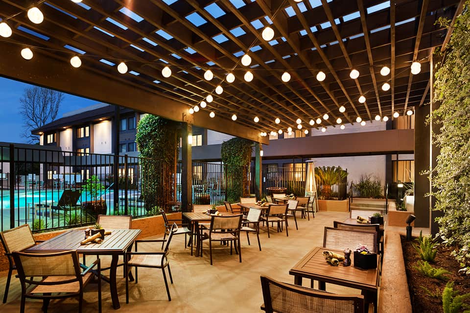 Upscale outdoor patio with pergola, string lights, lounge seating and illuminated pool view