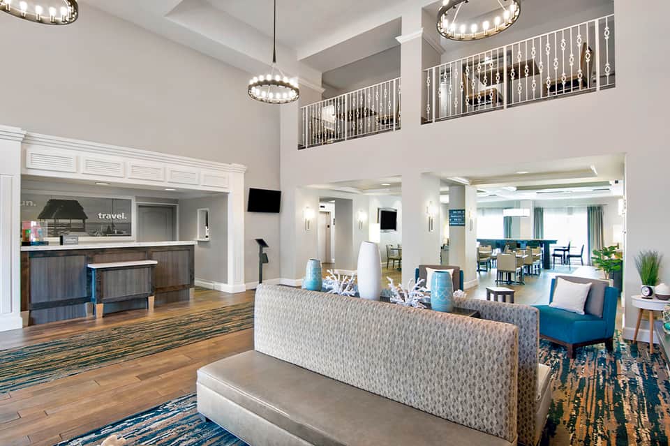 Modern hotel lobby with high ceilings, blue accent chairs, wooden floors, and front desk counter