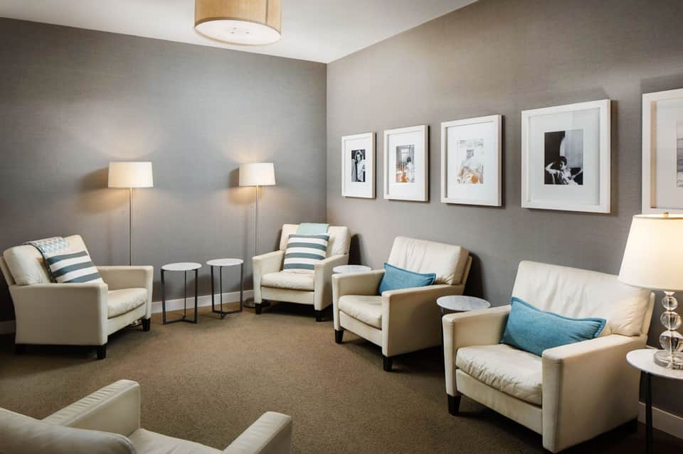 Elegant lounge with beige armchairs, striped pillows, framed artwork, and floor lamps on neutral carpet