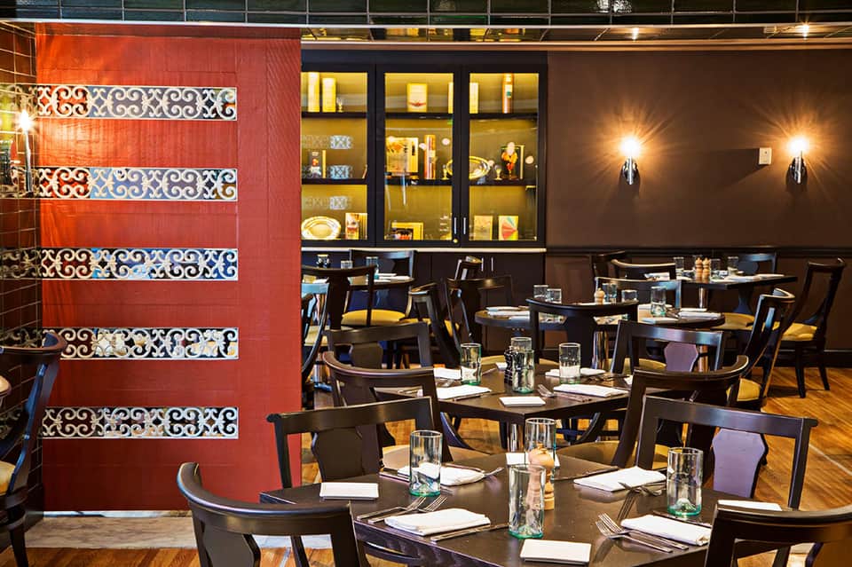Modern restaurant with red accent wall, decorative tile patterns, dark furniture, and warm lighting