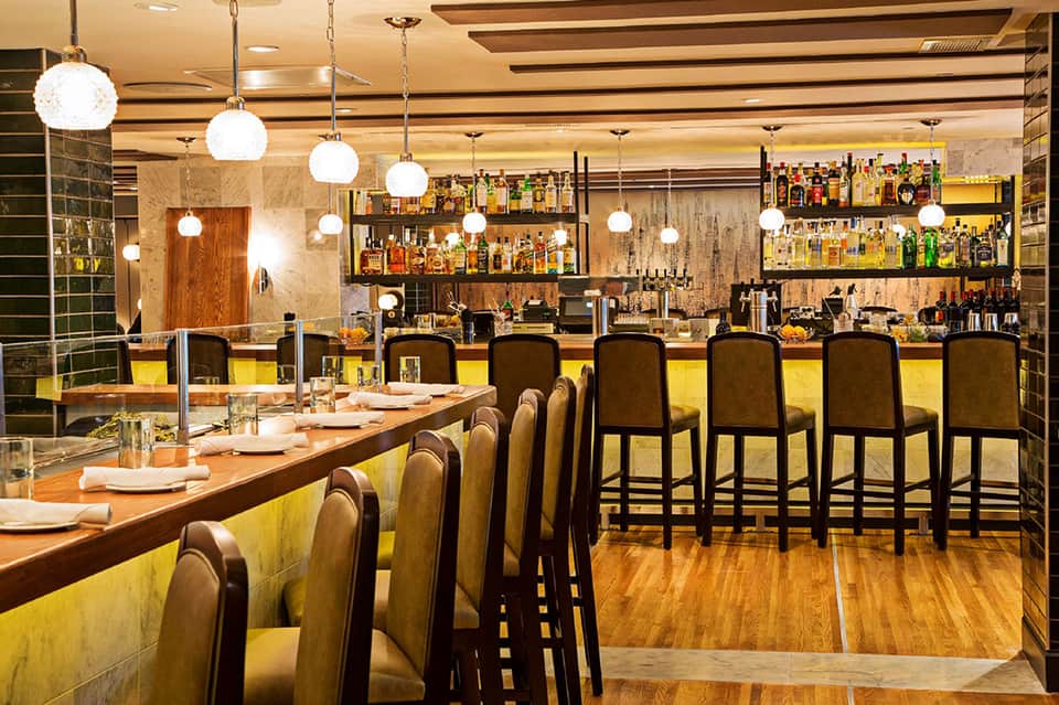 Contemporary bar and lounge with yellow accents, pendant lights, and full liquor shelves