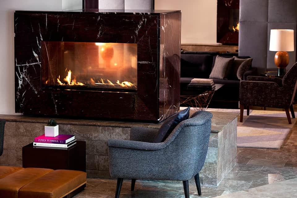 Luxury lounge with marble fireplace, gray armchair, dark sofa, and ambient firelight