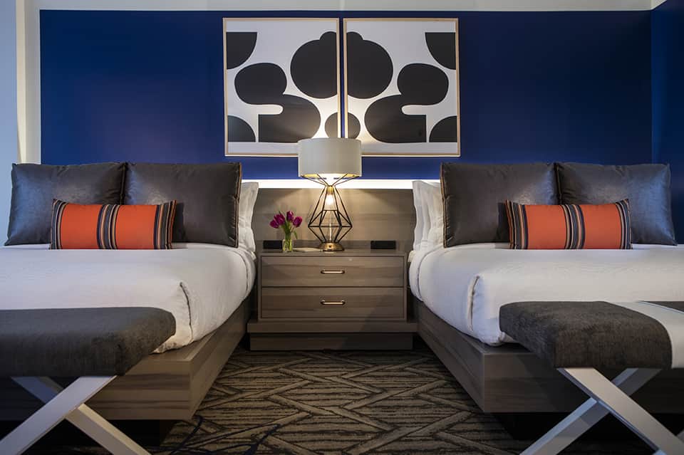 Upscale hotel bedroom with two beds, blue accent wall, modern artwork, and elegant furnishings