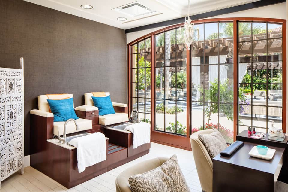 Luxury spa pedicure lounge with brown leather recliners, blue cushions, and floor-to-ceiling windows overlooking outdoor patio