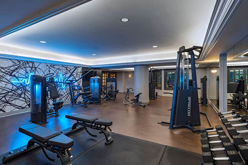 Modern fitness center with blue accent lighting, cardio equipment, strength machines, and mirrored walls