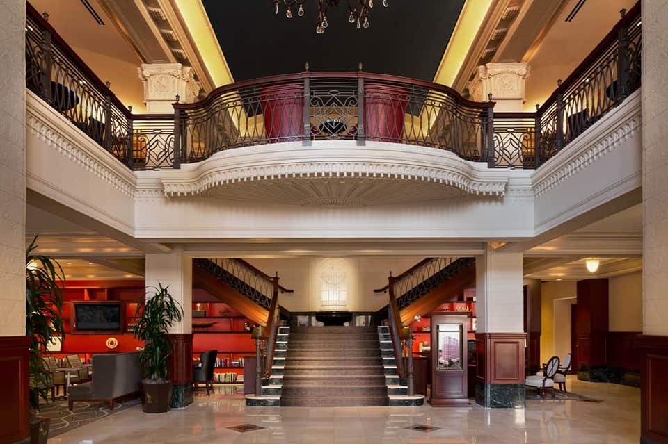 Grand hotel lobby with curved balcony, ornate railings, and symmetrical staircase