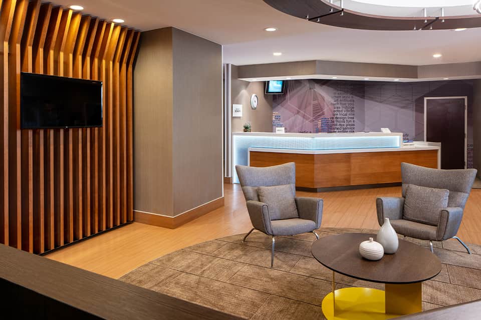 Modern hotel lobby with wooden slat accent wall, gray seating, reception desk with blue lighting