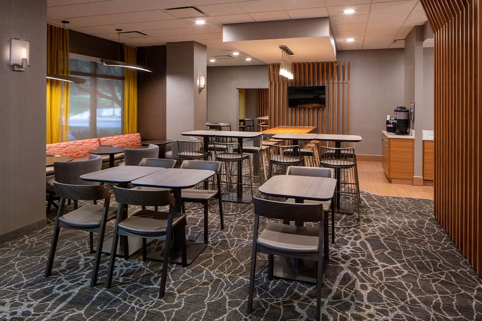 Hotel café and lounge area with wooden accent walls, tables, chairs, and yellow curtains