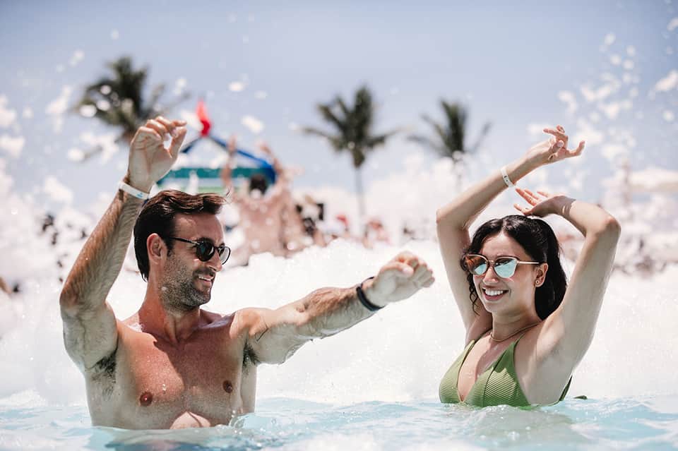 Couple swimming and celebrating in turquoise ocean water with palm trees and beach backdrop