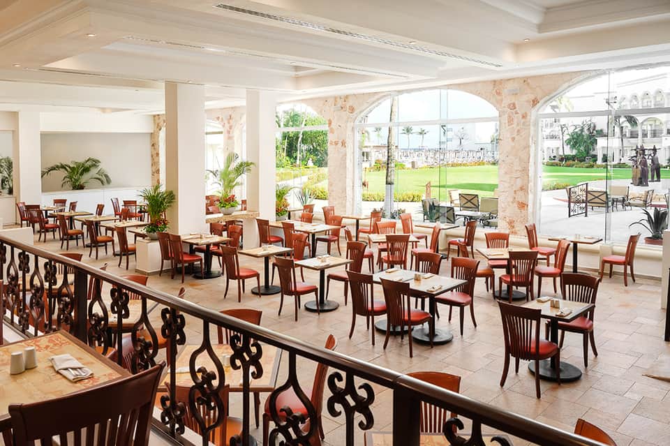 Elegant dining room with ornate railings, wooden chairs with orange cushions, and garden views