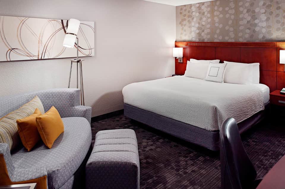 Modern hotel bedroom with red accent headboard, gray sofa, and contemporary furnishings