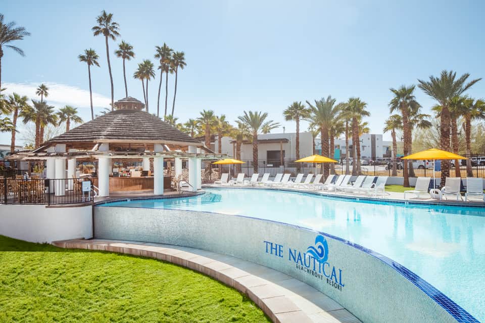 Expansive resort pool with cabana, palm trees, yellow umbrellas, and manicured lawn