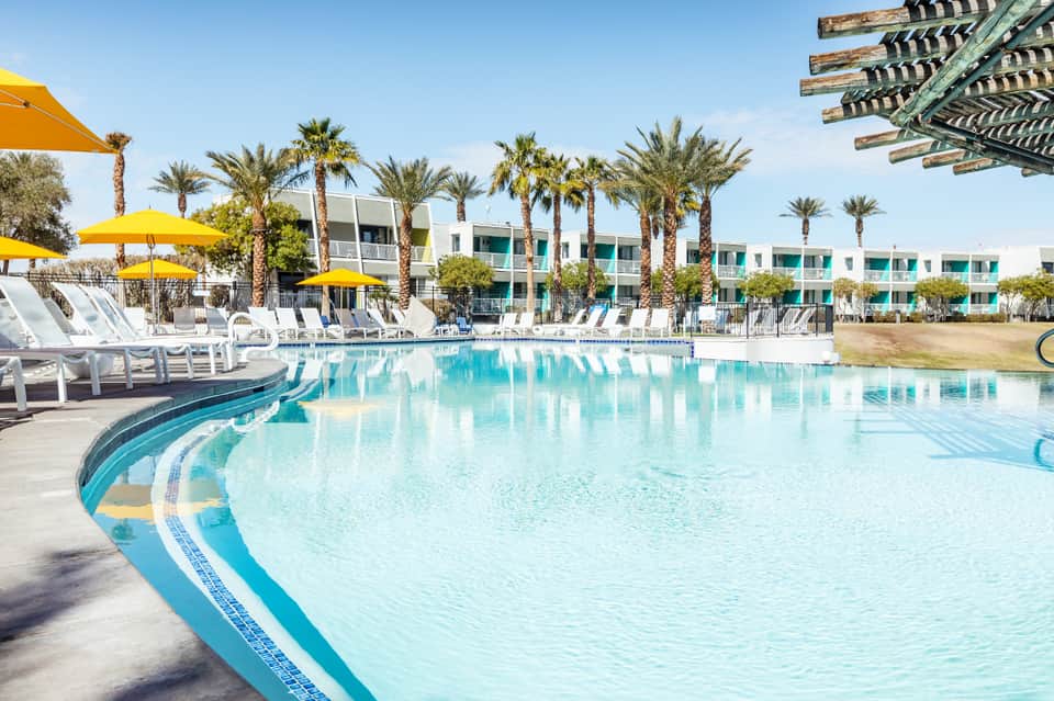 Resort pool with turquoise water, palm trees, yellow umbrellas, and modern accommodations