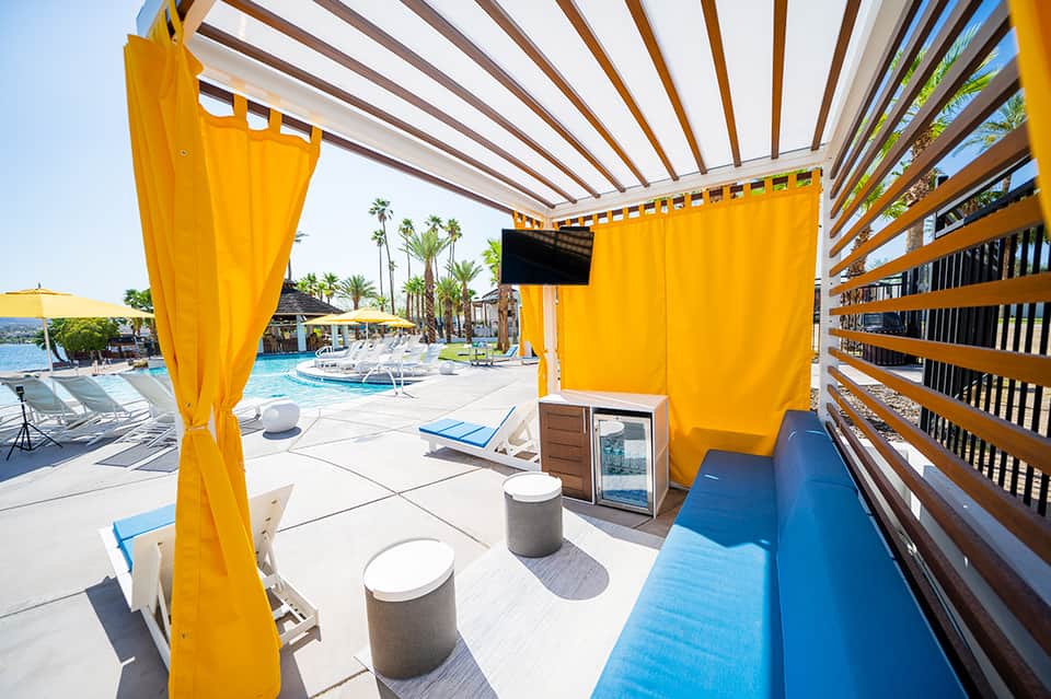 Pool area with bright yellow shade structures, lounge chairs, and palm tree backdrop