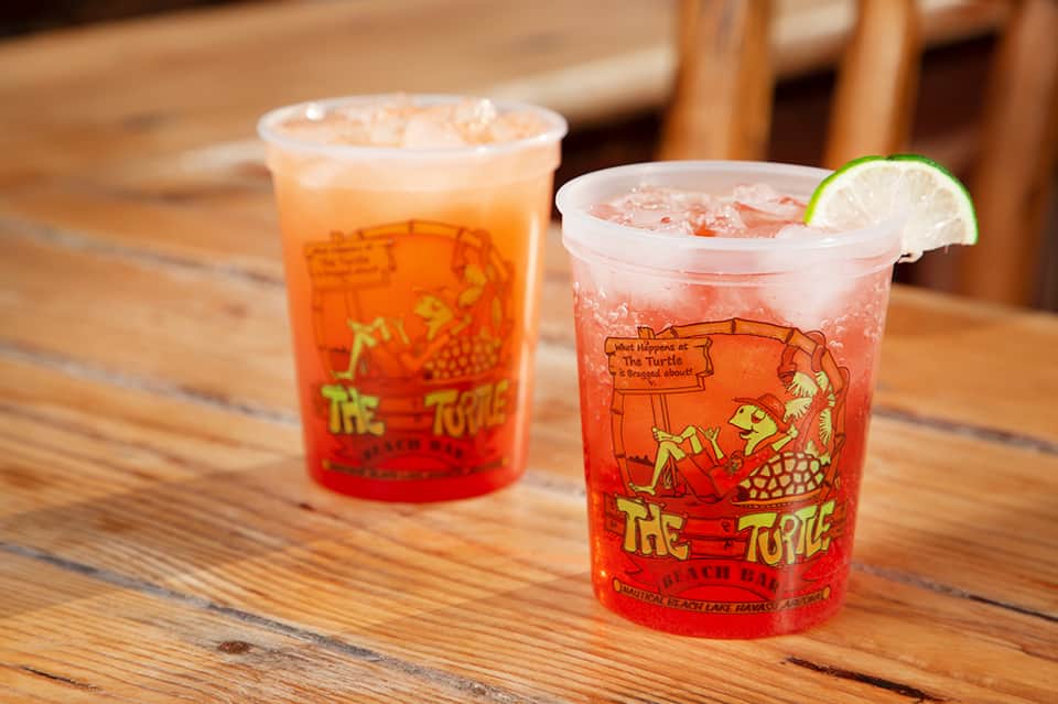 Two colorful red cocktails with lime garnish on wooden table at beachfront bar
