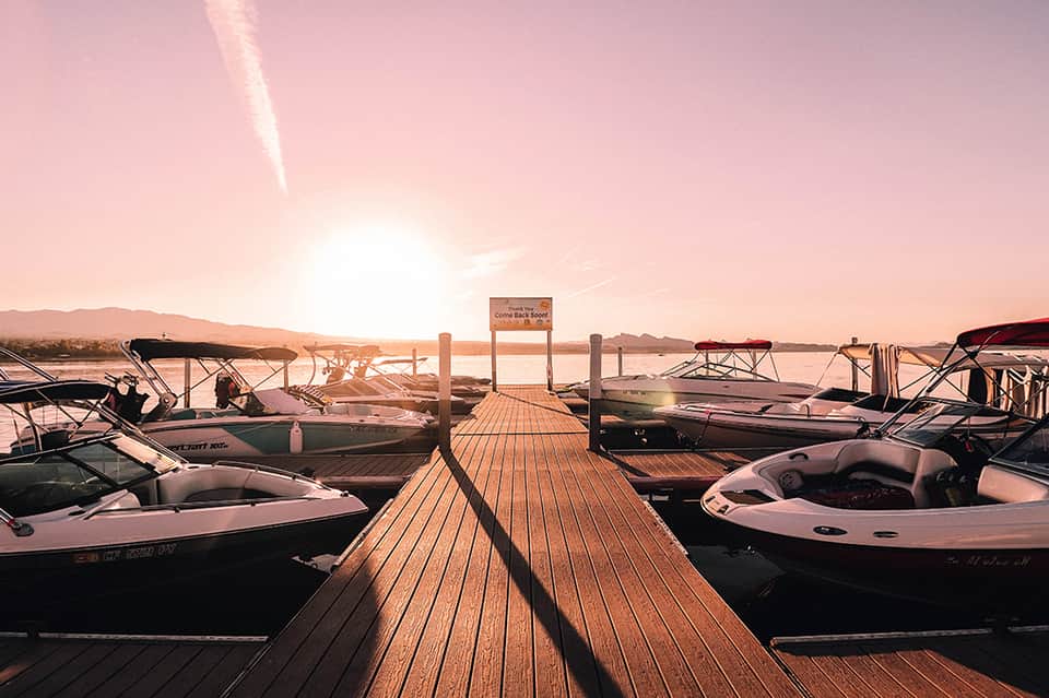 Sunset marina view with wooden dock, moored boats, calm water, and desert mountain landscape