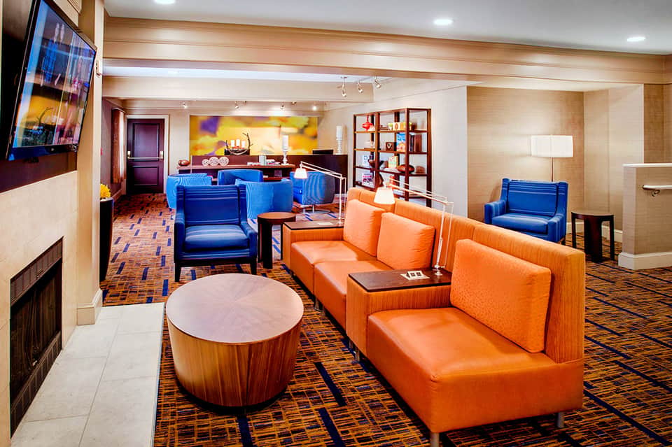 Modern hotel lounge with blue and orange seating, fireplace, wooden accents, and shelving