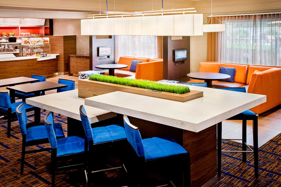 Modern hotel lobby with orange seating, blue chairs, natural elements, and casual dining area