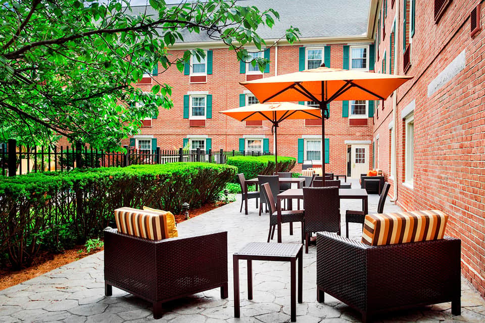 Courtyard seating area with orange umbrellas, brown wicker furniture, and brick historic building facade