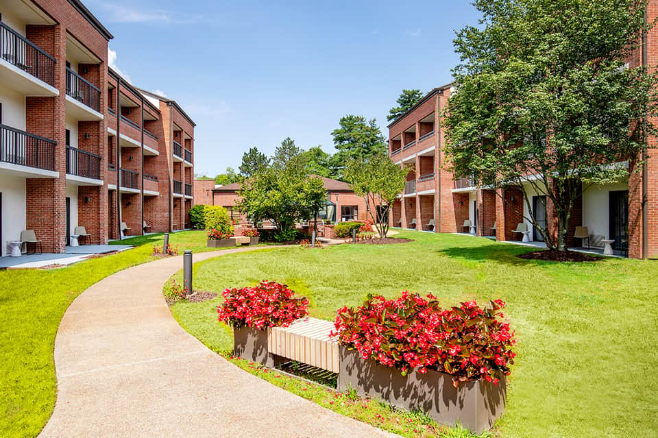 Brick residential courtyard with manicured lawn, red flowers, and curved walkway