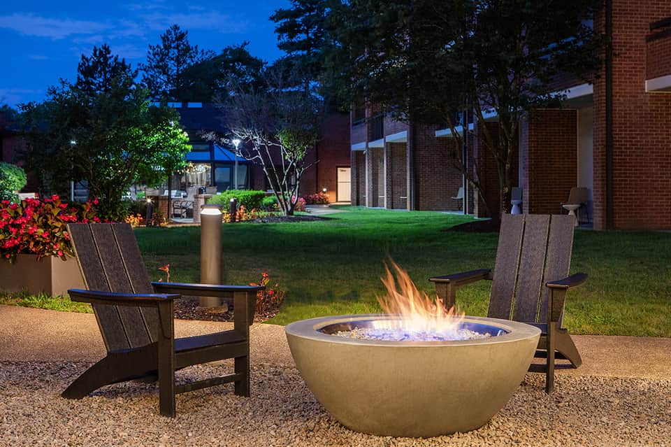 Evening fire pit with Adirondack chairs, landscaped grounds, and brick building architecture